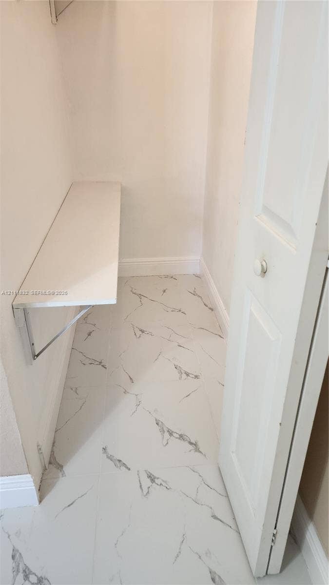 1250 SE 28th Court, #102, Homestead, FL 33035 Storage area featuring large-format tile flooring with a veined pattern, a built-in wall-mounted shelf, and a bi-fold door