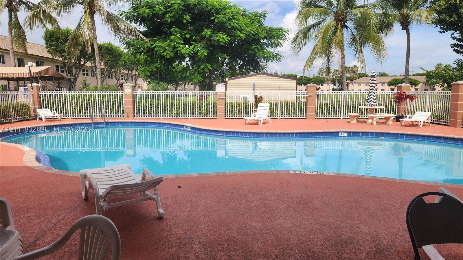 1250 SE 28th Court, #102, Homestead, FL 33035 In-ground swimming pool featuring a curved design, masonry pool decking, and a perimeter white metal fence with masonry pillars
