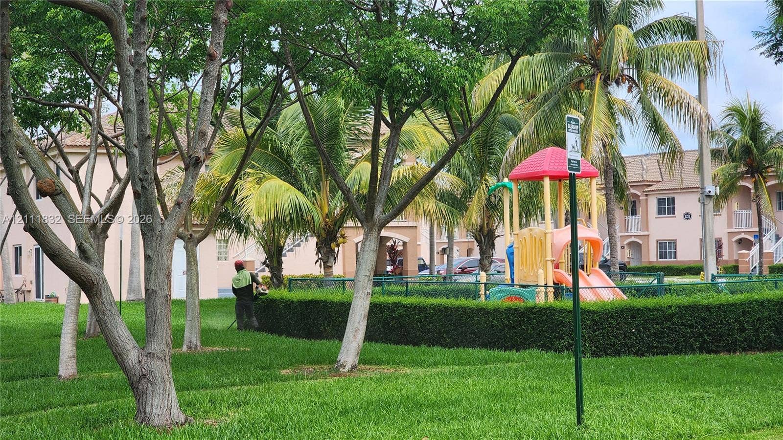 1250 SE 28th Court, #102, Homestead, FL 33035 Communal green space featuring manicured lawns, mature tropical landscaping, and a fenced playground structure