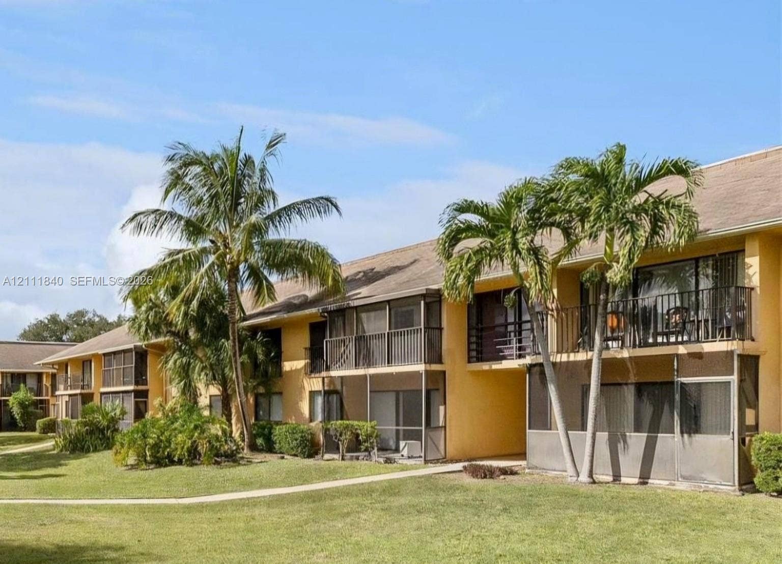 5901 Washington Street, #250, Hollywood, FL 33023 Stucco exterior featuring screened-in lanais, private balconies with metal railings, and mature palm trees situated on landscaped grounds