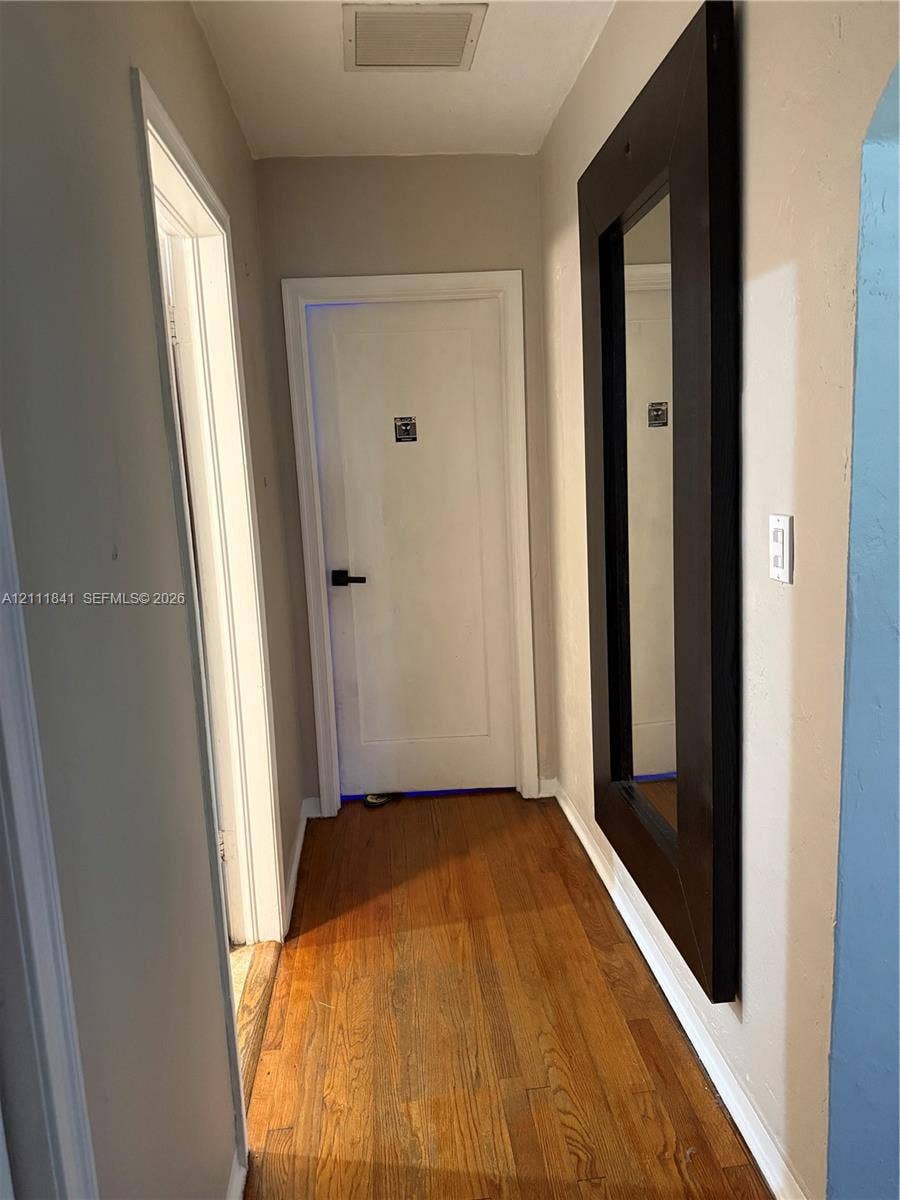 12015 NE 6th Avenue, Biscayne Park, FL 33161 Hallway featuring wood-finish flooring, white panel door with matte black hardware, and wall-mounted dark-toned frame