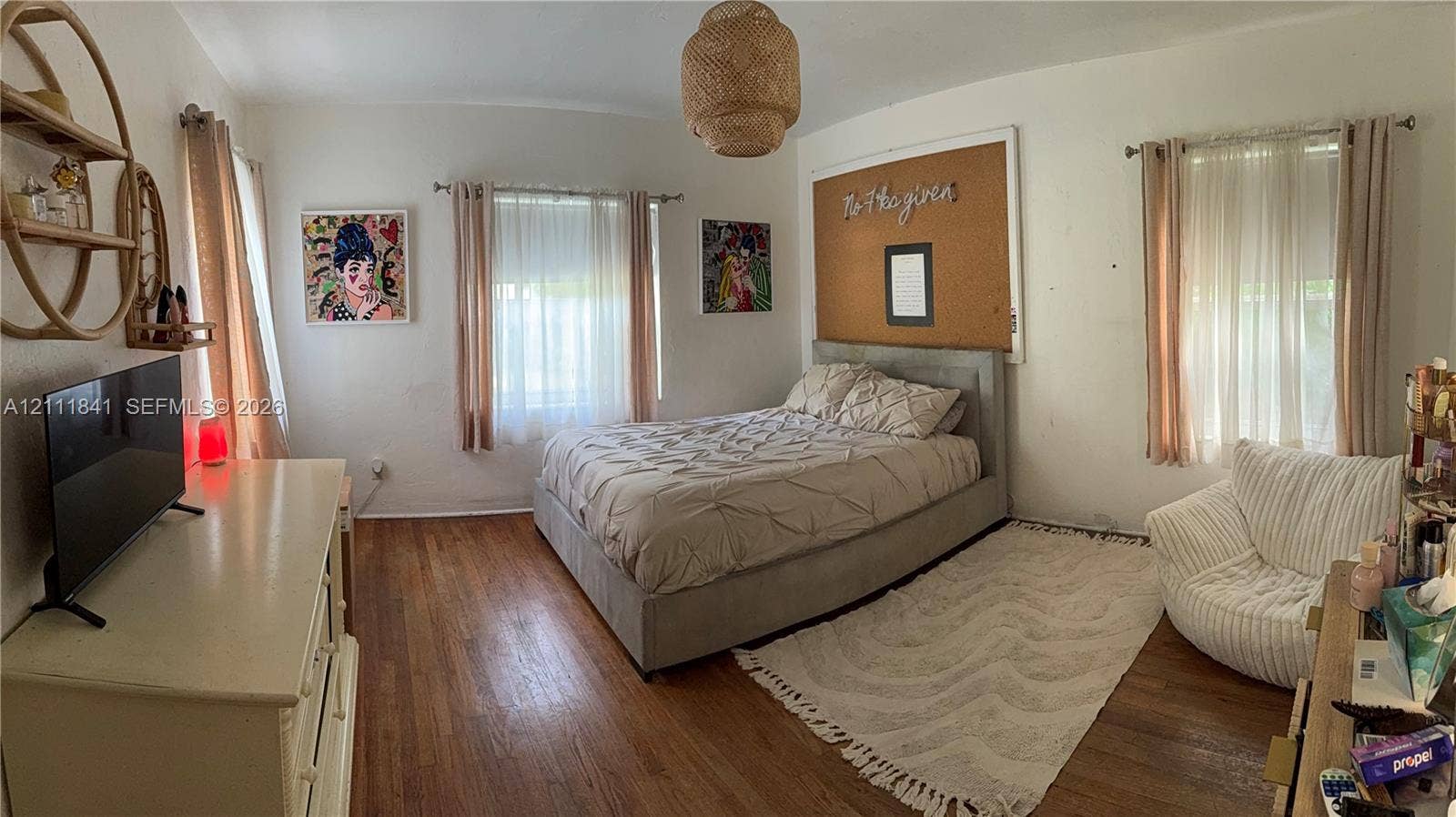 12015 NE 6th Avenue, Biscayne Park, FL 33161 Bedroom featuring wood-finish flooring, two windows with adjustable window treatments, and a hanging woven light fixture