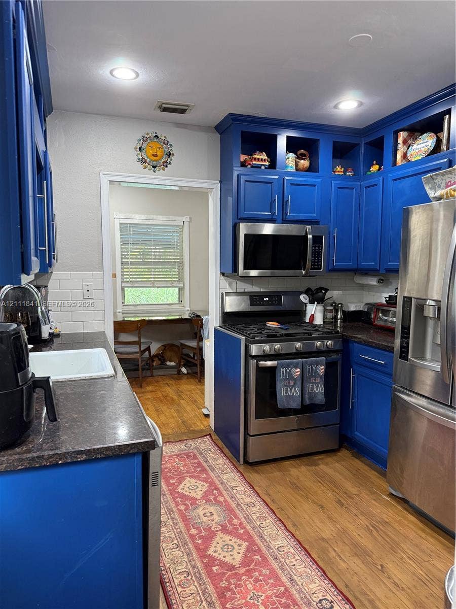 12015 NE 6th Avenue, Biscayne Park, FL 33161 Kitchen featuring custom blue cabinetry, stone-finish countertops, white subway tile backsplash, recessed lighting, and stainless steel appliances