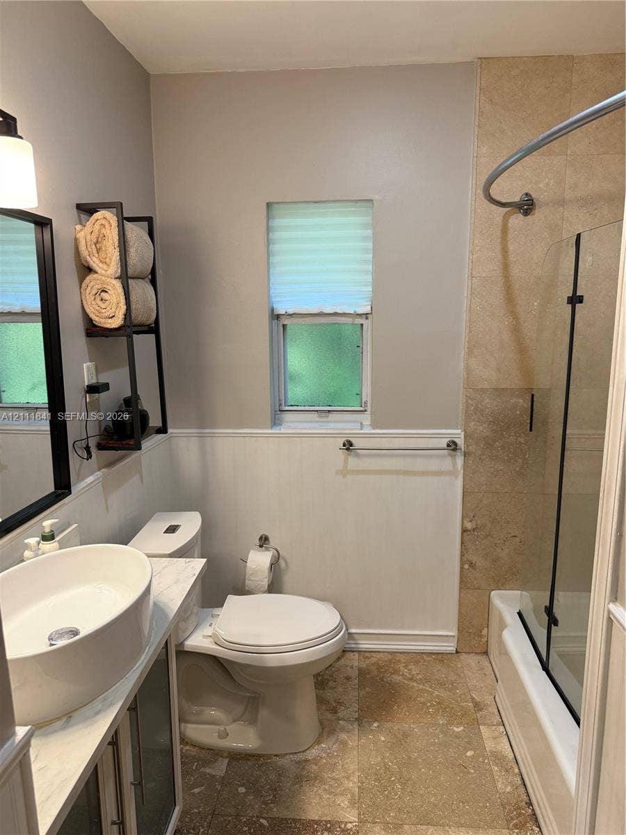 12015 NE 6th Avenue, Biscayne Park, FL 33161 Bathroom featuring a vessel sink with a stone-top vanity, tile flooring, glass shower panel with a curved curtain rod, and wainscoting