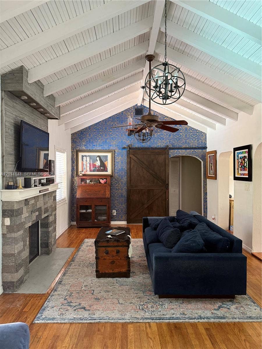 12015 NE 6th Avenue, Biscayne Park, FL 33161 Vaulted ceiling with exposed white beams, stone-surround fireplace, wood-finish flooring, and sliding wood barn door