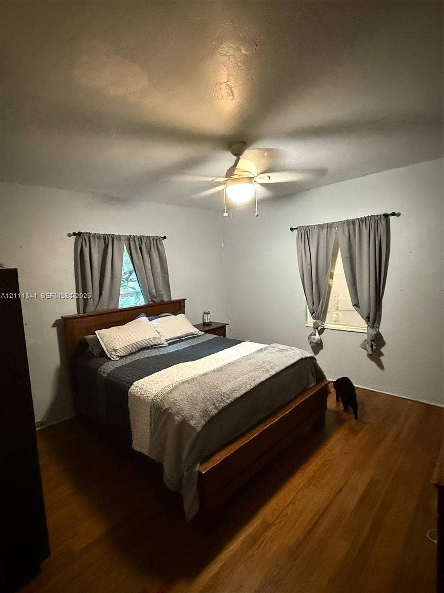 12015 NE 6th Avenue, Biscayne Park, FL 33161 Room featuring wood-finish flooring, two windows with curtain rods, and a ceiling fan with integrated lighting