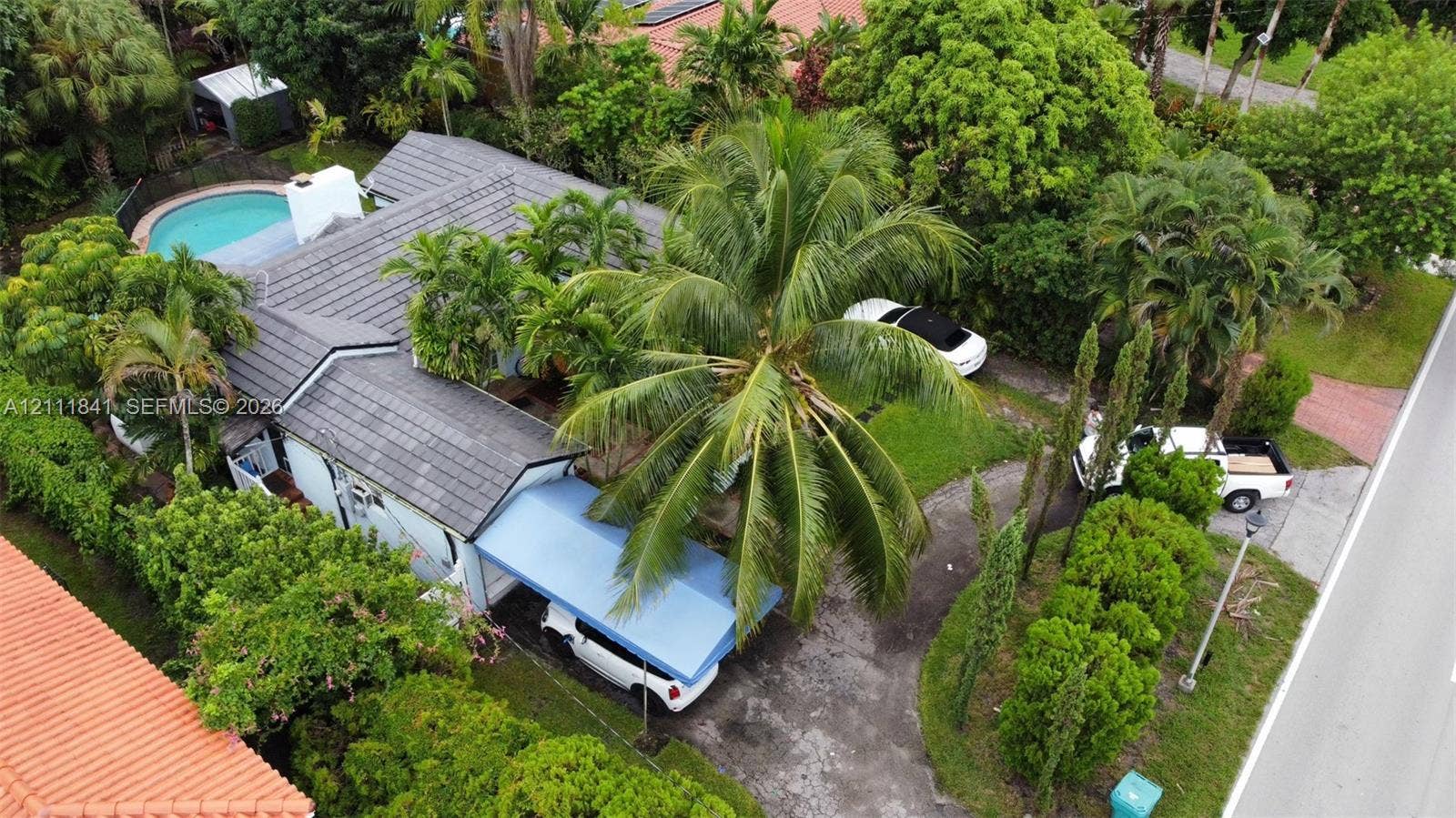 12015 NE 6th Avenue, Biscayne Park, FL 33161 Aerial perspective of a property featuring a tile roof, an outdoor swimming pool, a covered carport, and mature landscaping