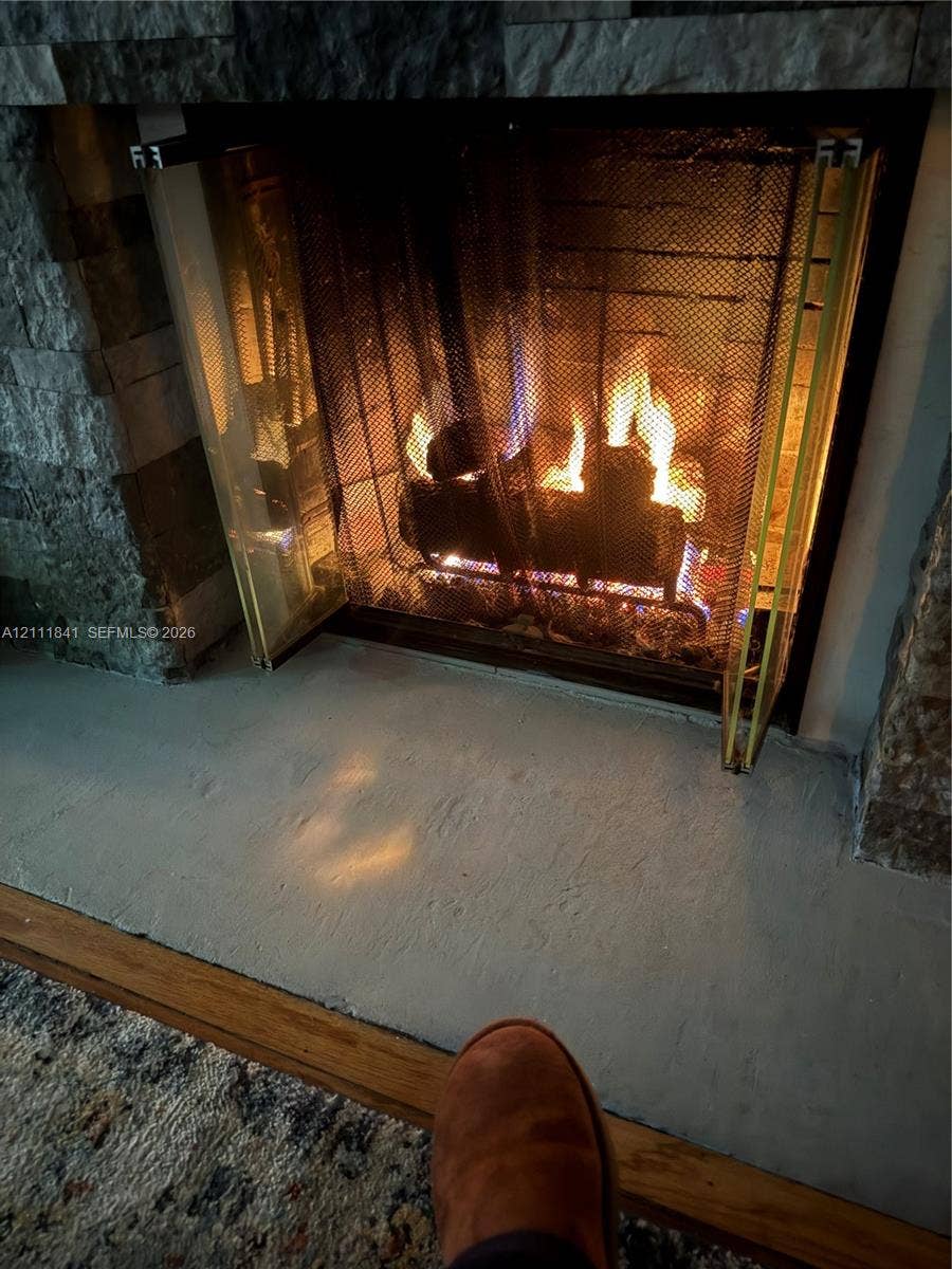 12015 NE 6th Avenue, Biscayne Park, FL 33161 Fireplace featuring a multi-tonal stacked stone surround, metal mesh screen, and a solid hearth