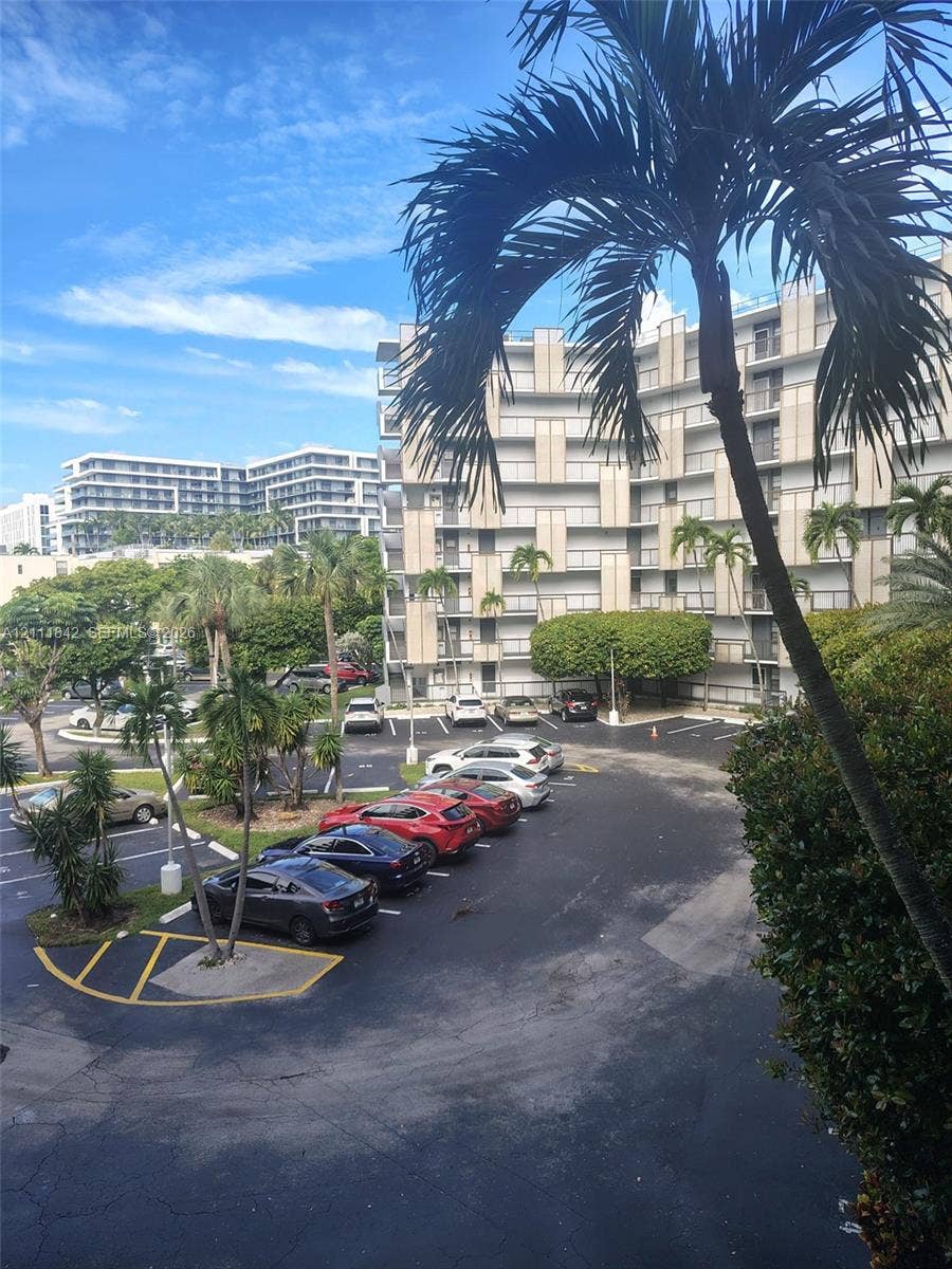 20400 W Country Club Drive, #303, Aventura, Aventura, FL 33180 Multi-story building featuring concrete balconies, landscaped grounds with palm trees, and paved surface parking