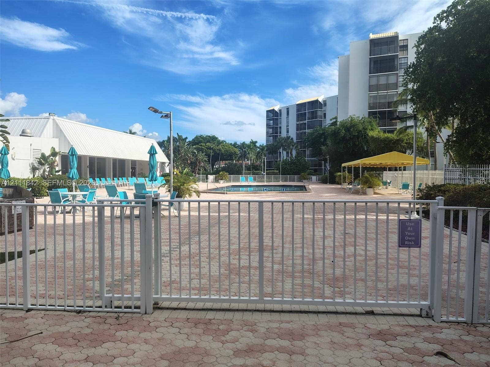 20400 W Country Club Drive, #303, Aventura, Aventura, FL 33180 Community pool area featuring paver decking, white metal security fencing, and a yellow-canopied pavilion