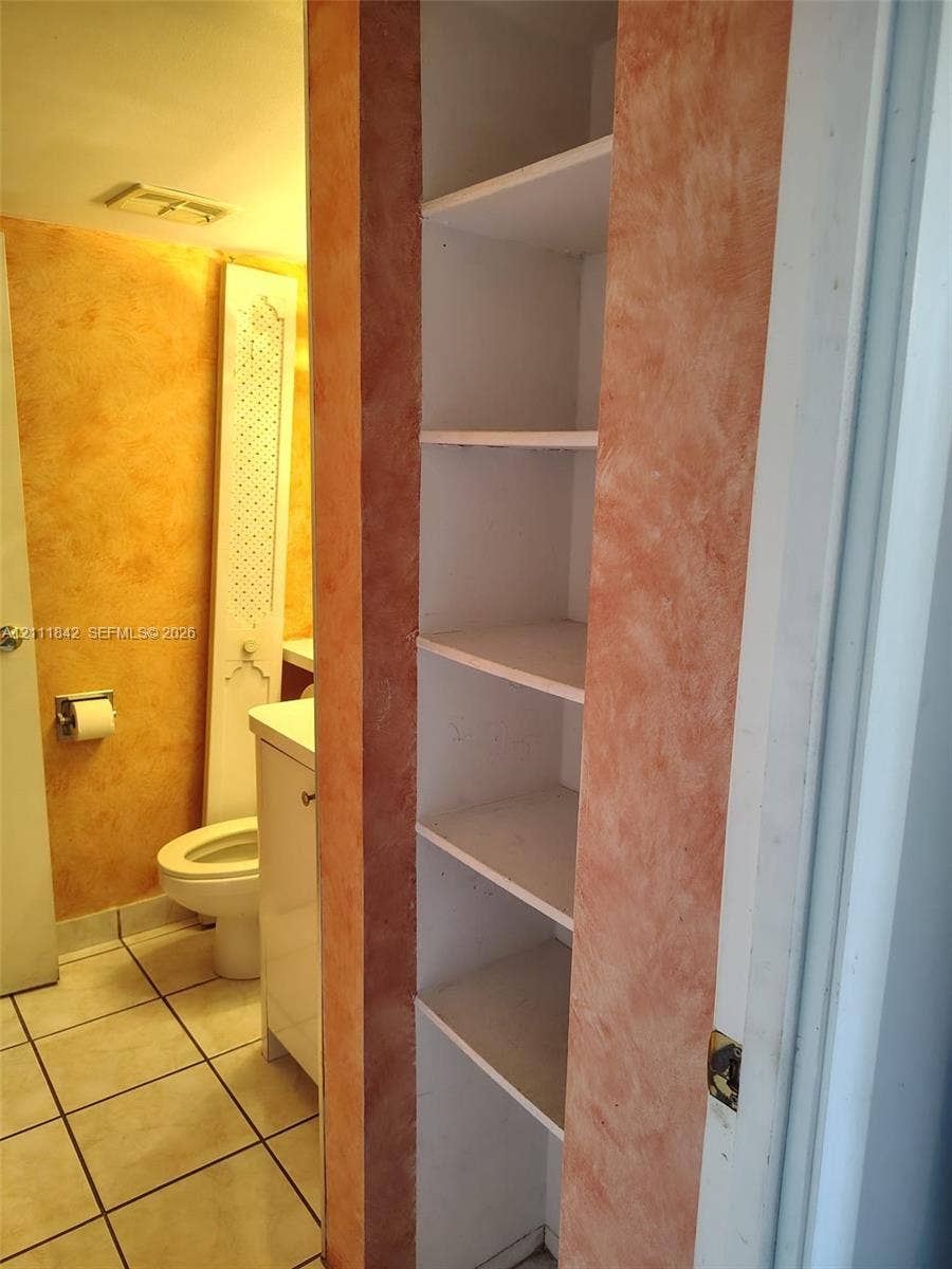 20400 W Country Club Drive, #303, Aventura, Aventura, FL 33180 Built-in floor-to-ceiling storage shelving with a decorative faux-finish trim, ceramic tile flooring, and a white vanity cabinet