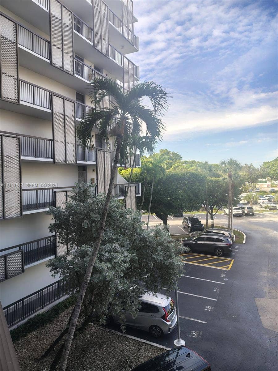 20400 W Country Club Drive, #303, Aventura, Aventura, FL 33180 High-rise building exterior featuring tiered balconies with decorative metal privacy screens, mature palm trees, and ground-level parking