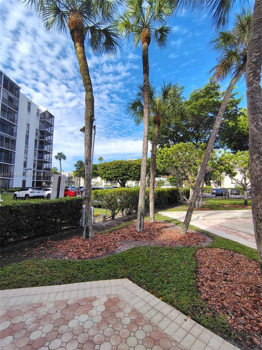 20400 W Country Club Drive, #303, Aventura, Aventura, FL 33180 Landscaped grounds featuring mature palm trees, manicured hedges, patterned paver hardscaping, and defined mulch beds