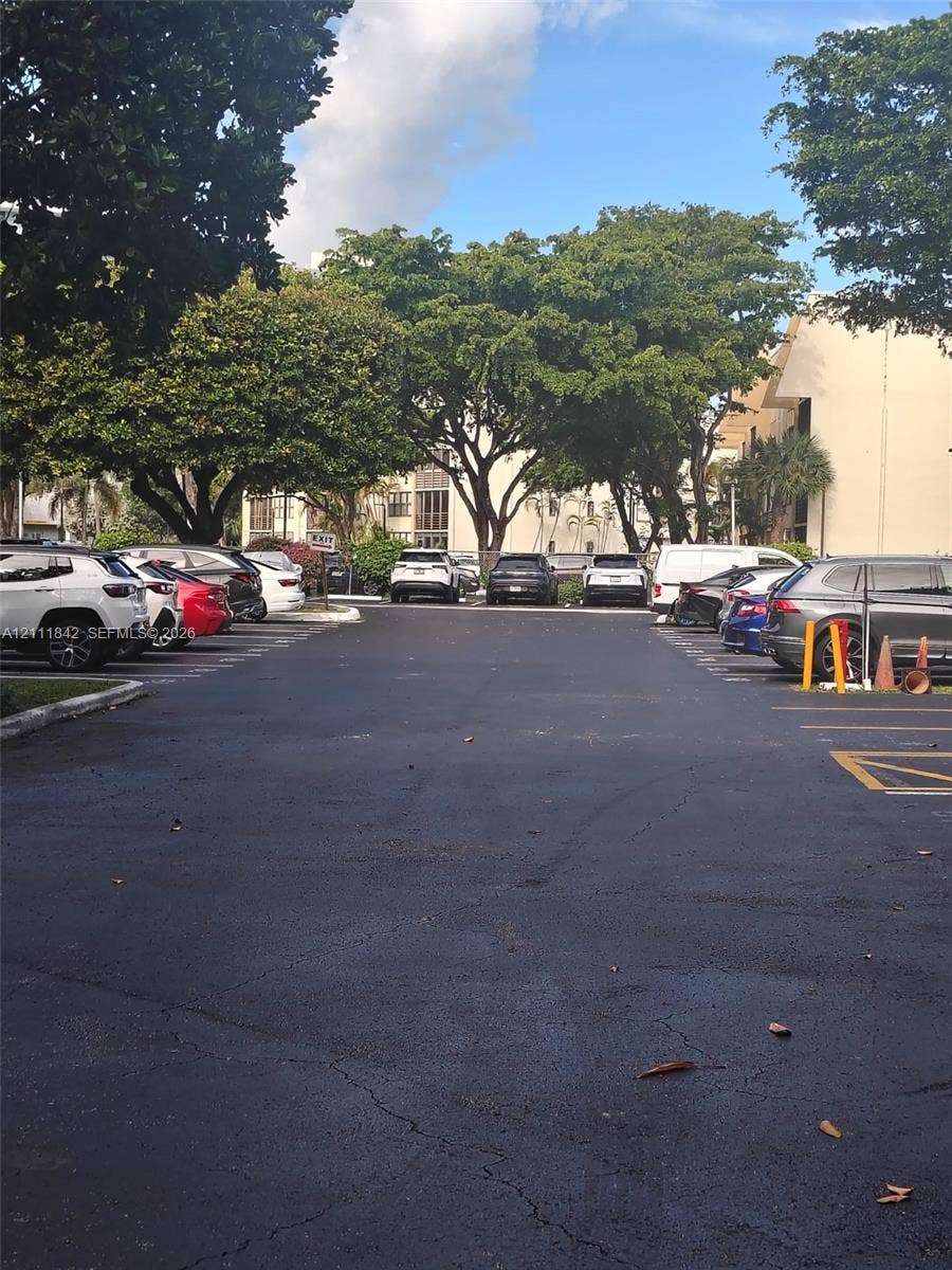 20400 W Country Club Drive, #303, Aventura, Aventura, FL 33180 Asphalt-paved parking lot featuring designated parking stalls, mature trees, and perimeter landscaping