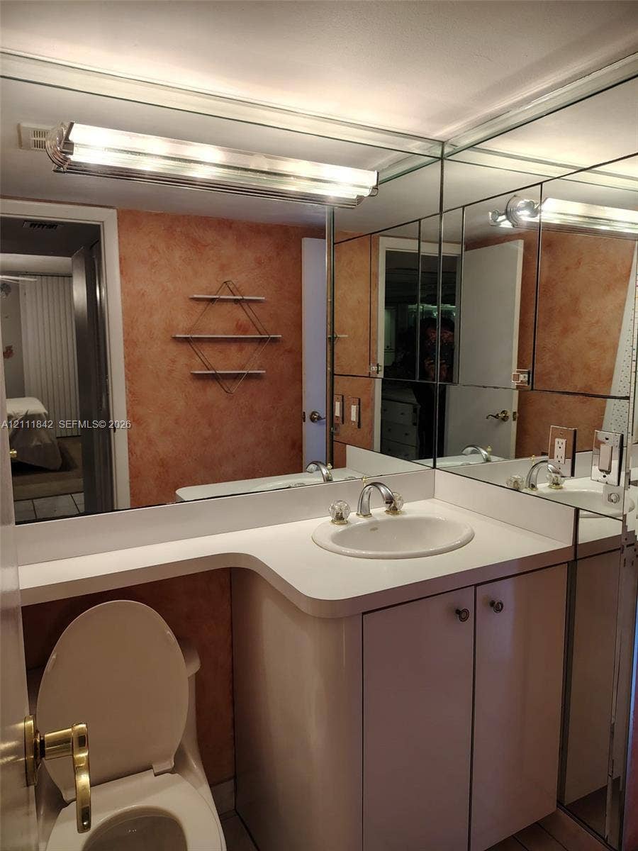 20400 W Country Club Drive, #303, Aventura, Aventura, FL 33180 Bathroom vanity featuring a solid surface countertop, integrated sink with dual-handle faucet, white cabinetry, and a large-scale mirrored wall