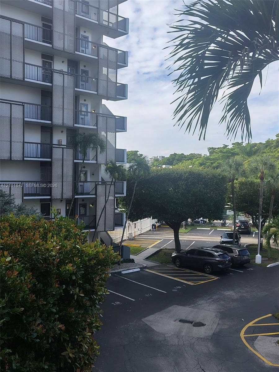 20400 W Country Club Drive, #303, Aventura, Aventura, FL 33180 Multi-story building exterior featuring staggered balconies with metal mesh privacy screening, dedicated asphalt parking area, and mature palm landscaping