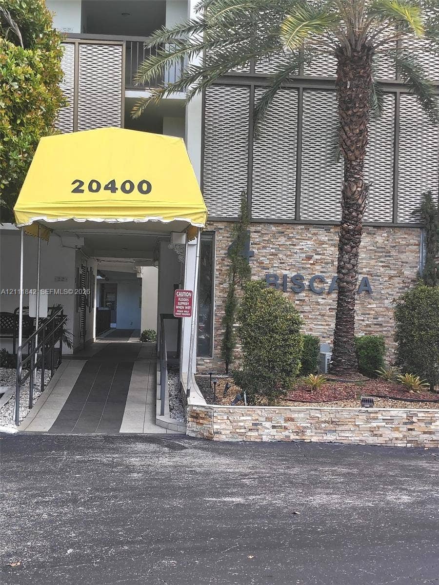 20400 W Country Club Drive, #303, Aventura, Aventura, FL 33180 Building exterior featuring stone masonry facade, decorative metal screening, concrete access ramp, and metal awning