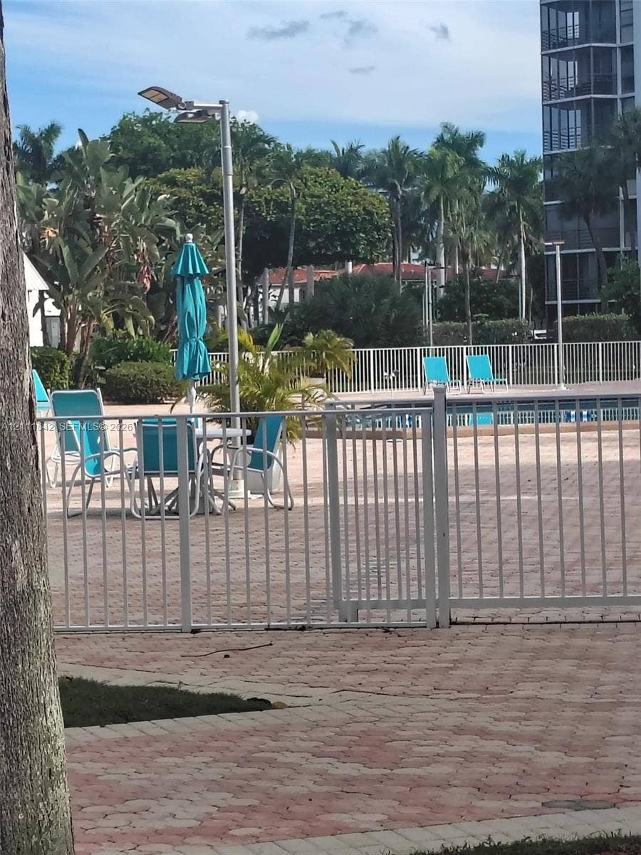 20400 W Country Club Drive, #303, Aventura, Aventura, FL 33180 Swimming pool area featuring a paver stone deck, white metal perimeter fencing, and established palm tree landscaping