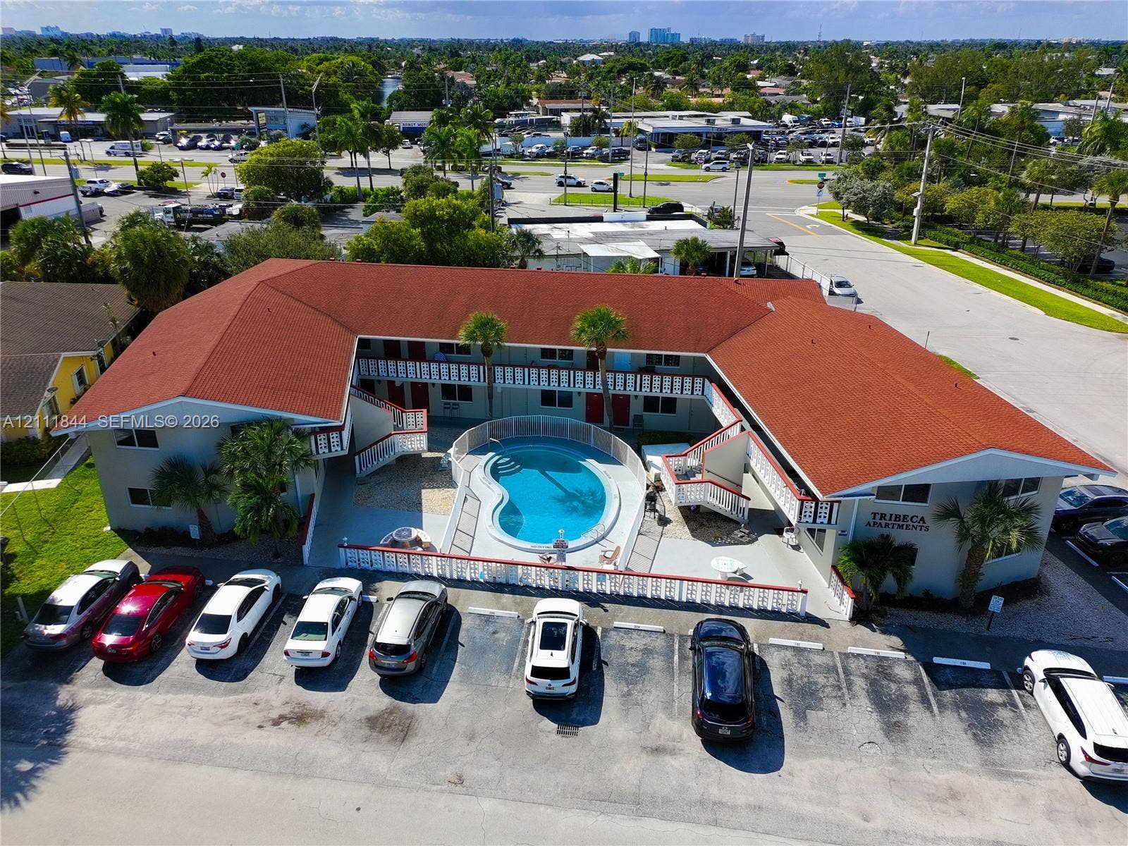 U-shaped apartment complex featuring a central courtyard swimming pool, exterior staircases, asphalt-paved surface parking, and red shingle roofing