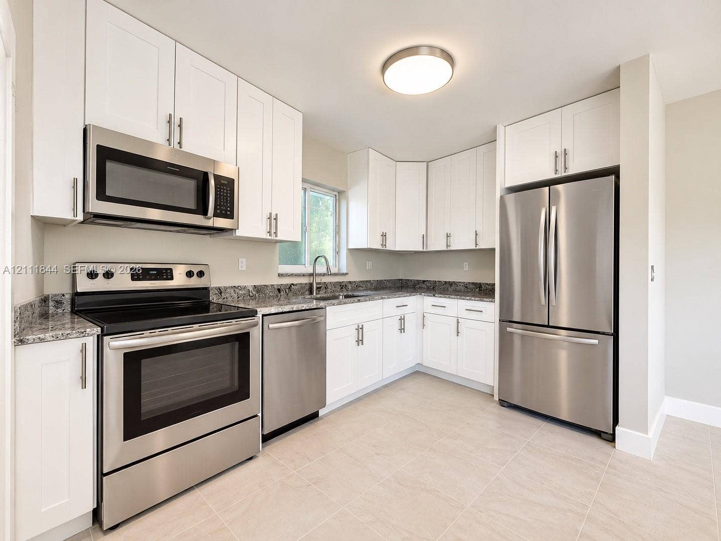 Kitchen featuring white Shaker-style cabinetry, stone-finish countertops, stainless steel appliances, a dual-basin undermount sink, and tile flooring