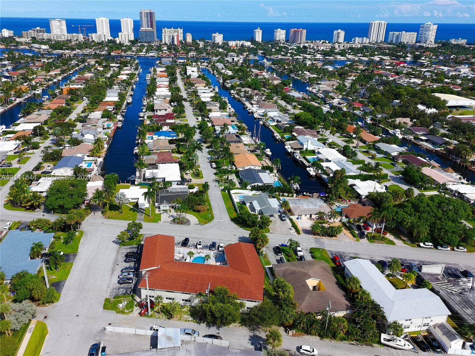 Aerial perspective featuring a multi-unit building with a clay tile roof, a central courtyard swimming pool, and an urban coastal location