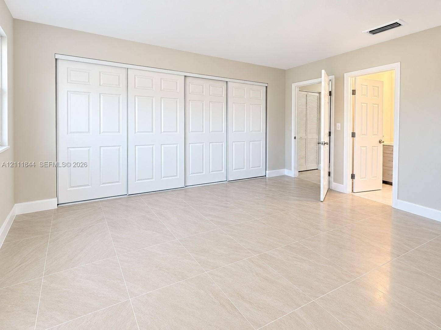 Neutral-toned interior space featuring light-colored stone-finish tile flooring, four-panel sliding closet doors, and traditional hinged doorways with brushed metal hardware