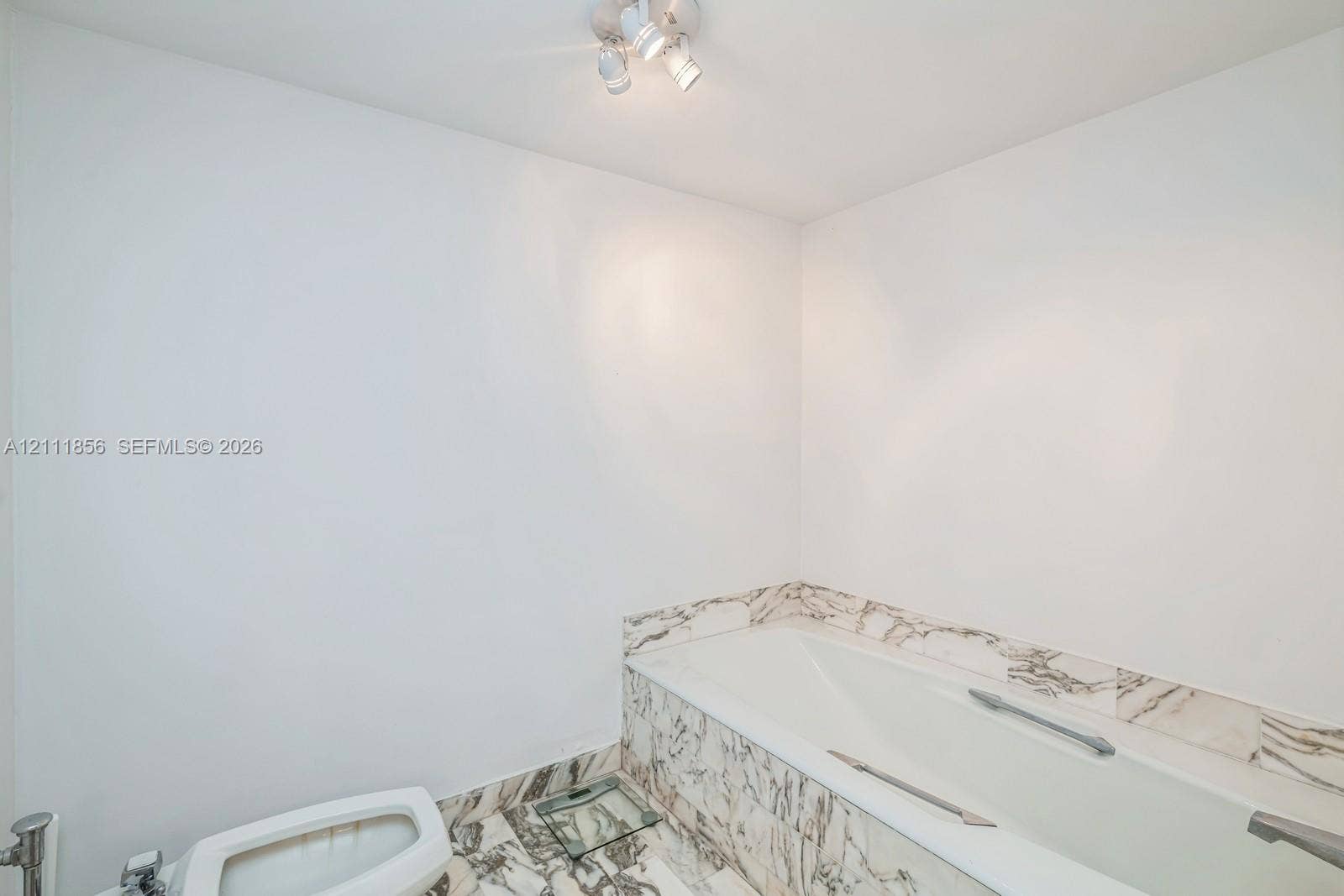 6423 Collins Avenue, #1602, Miami Beach, FL 33141 Bathtub featuring stone-patterned tile surround and flooring, accompanied by polished chrome hardware and a ceiling-mounted spotlight fixture