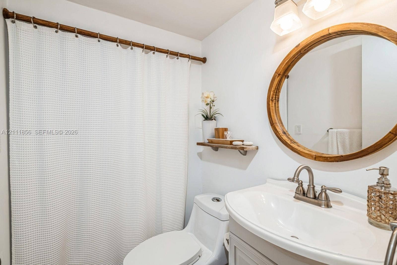 6423 Collins Avenue, #1602, Miami Beach, FL 33141 Bathroom vanity with a white basin and metallic faucet, circular wood-framed mirror, dual-bulb wall-mounted light fixture, and wooden wall-mounted shelving