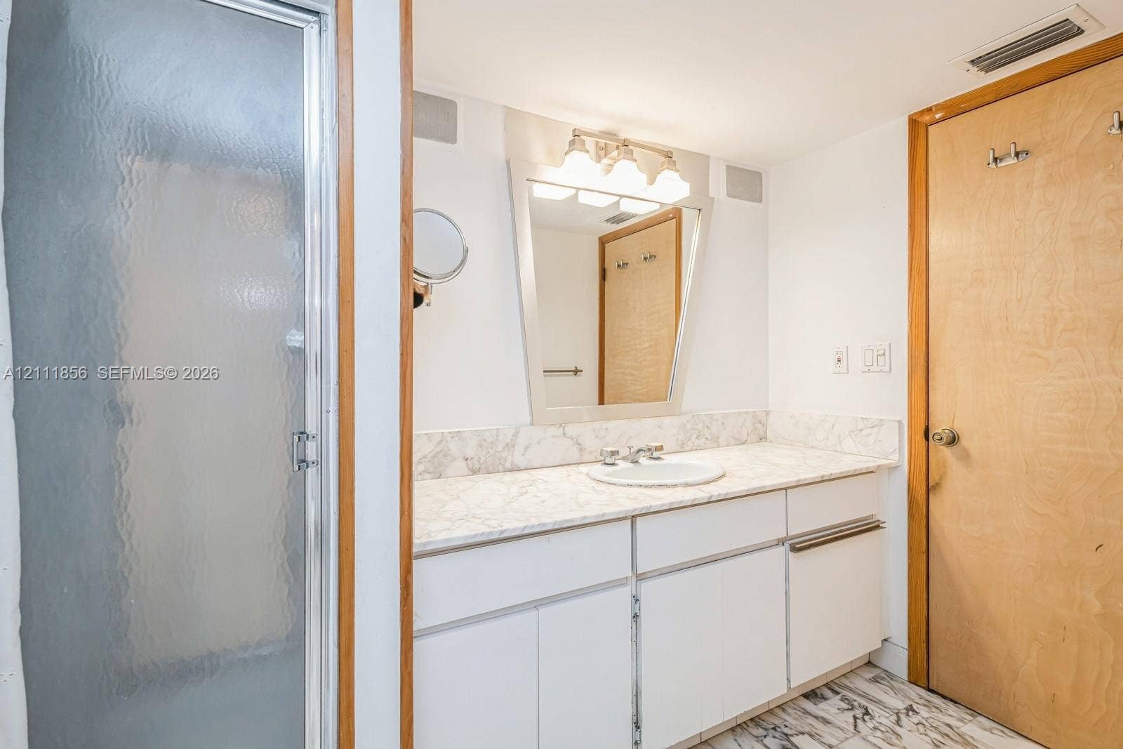 6423 Collins Avenue, #1602, Miami Beach, FL 33141 Bathroom featuring a vanity with stone-finish countertop, integrated sink, framed wall mirror with multi-bulb overhead lighting, stone-patterned flooring, and a glass-enclosed shower