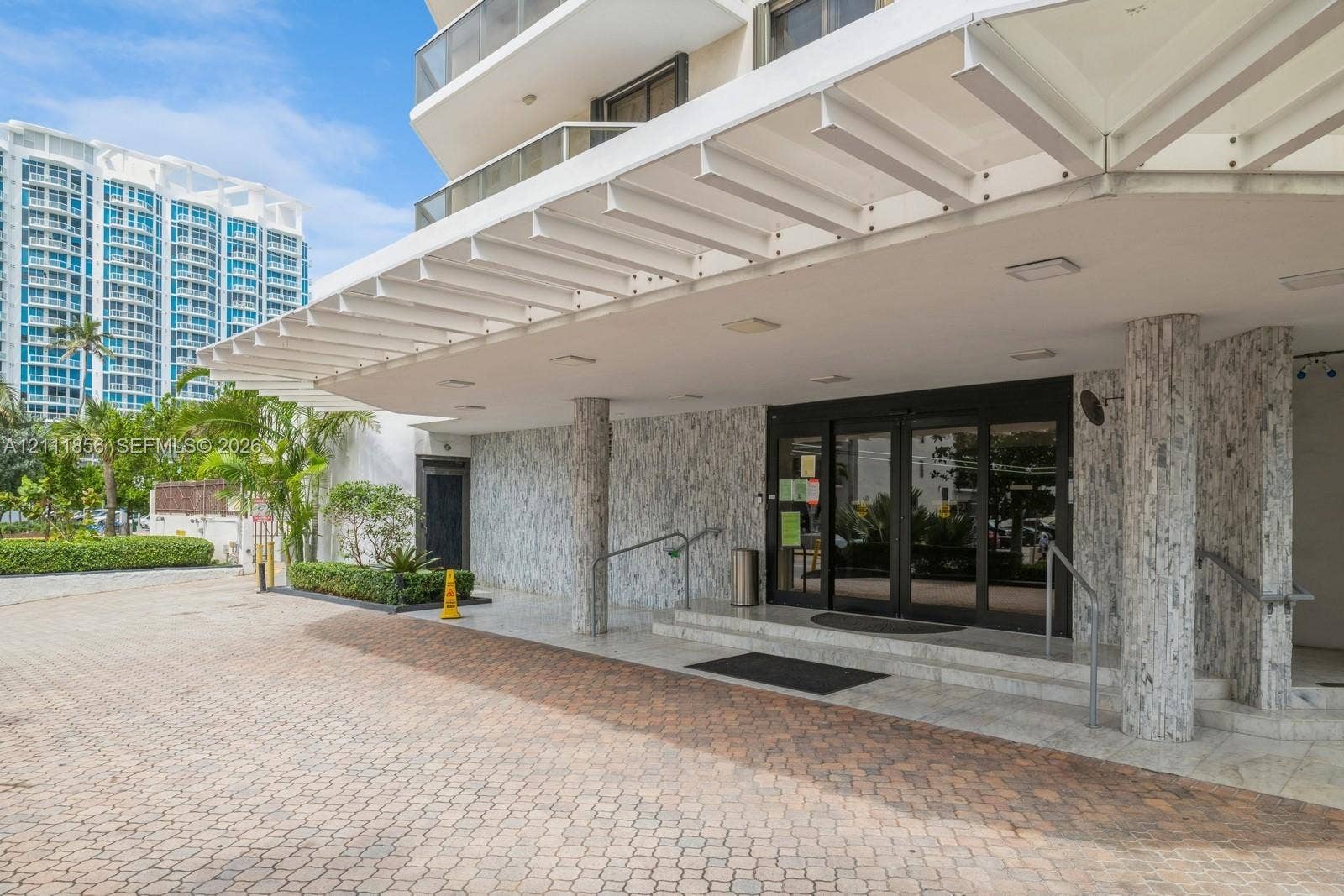 6423 Collins Avenue, #1602, Miami Beach, FL 33141 Covered entrance featuring a stone-clad facade, paver driveway, recessed lighting, and metal handrails