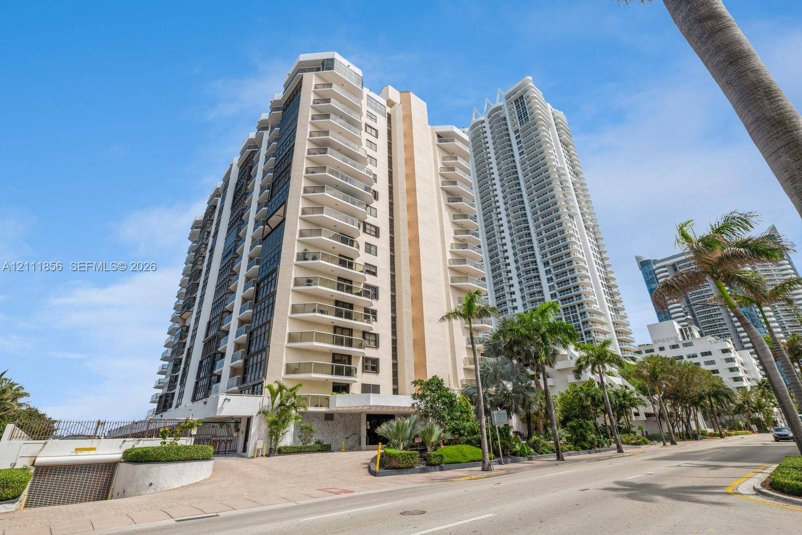 6423 Collins Avenue, #1602, Miami Beach, FL 33141 High-rise residential exterior featuring stacked private balconies, concrete construction, street-level covered parking access, and tropical landscaping