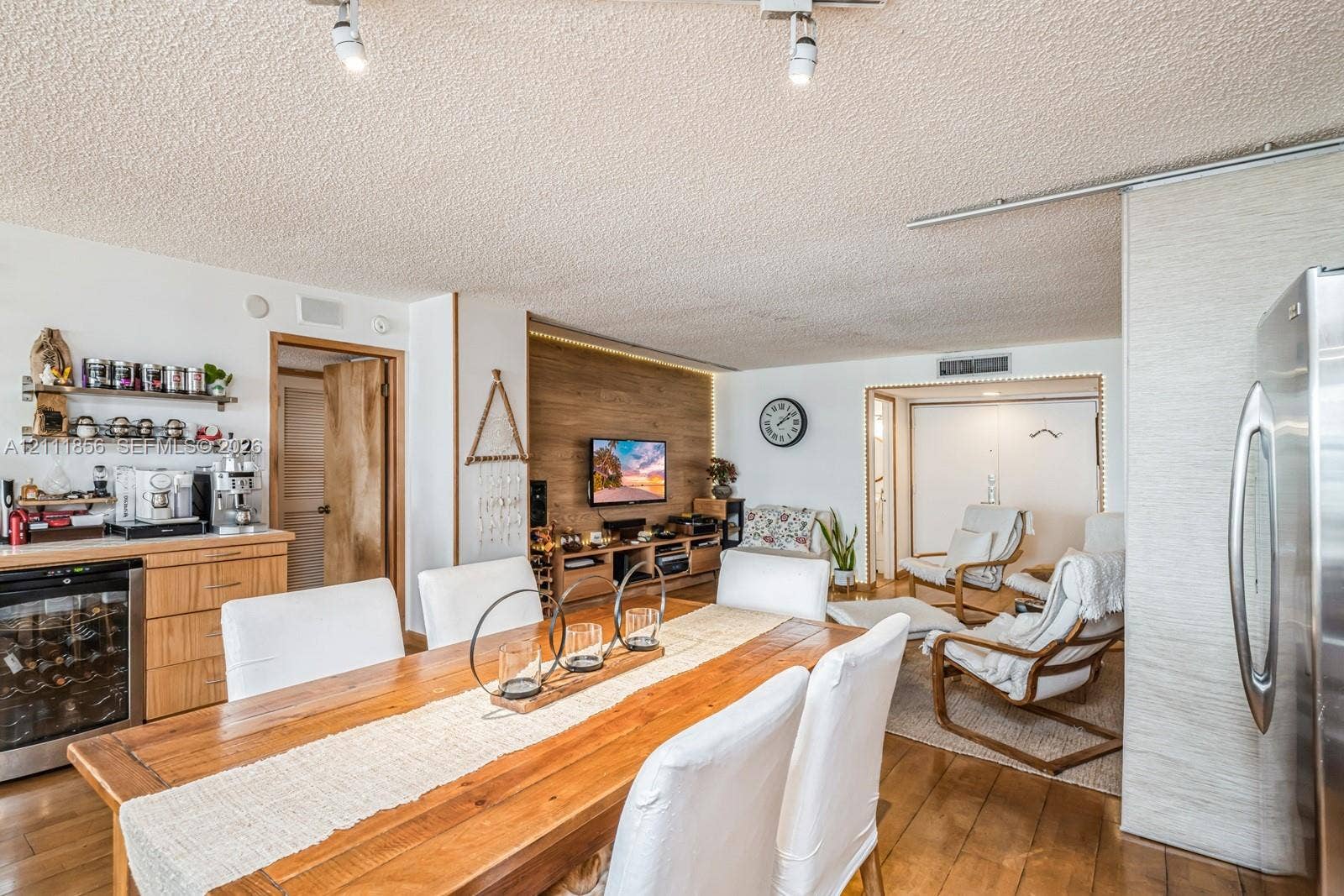 6423 Collins Avenue, #1602, Miami Beach, FL 33141 Open-concept interior featuring wood-finish flooring, a wood-paneled accent wall with integrated cove lighting, custom built-in cabinetry, and a glass-front beverage cooler