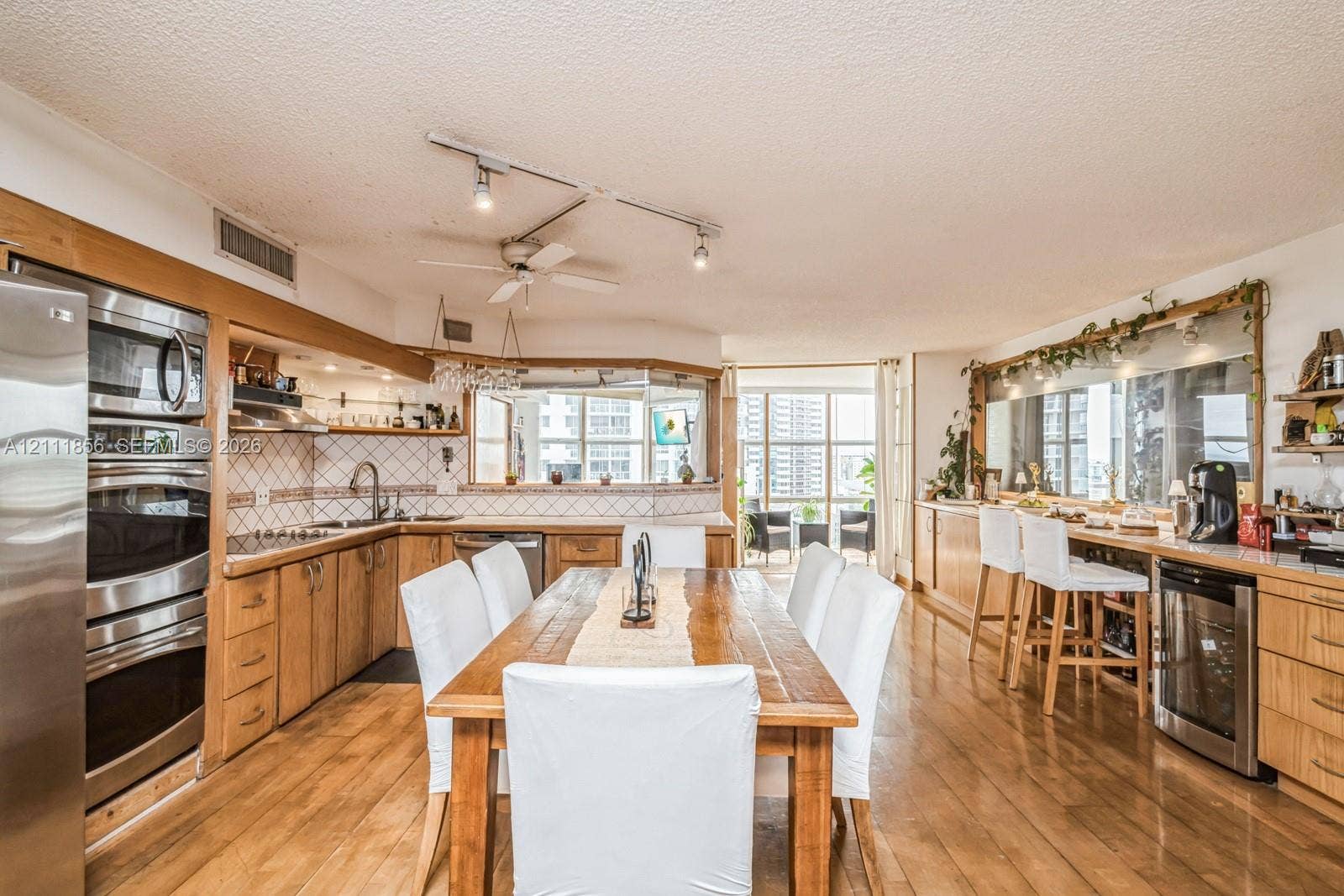 6423 Collins Avenue, #1602, Miami Beach, FL 33141 Kitchen featuring wood cabinetry, stainless steel double wall ovens, a dedicated wine refrigerator, track lighting, and wood-finish flooring