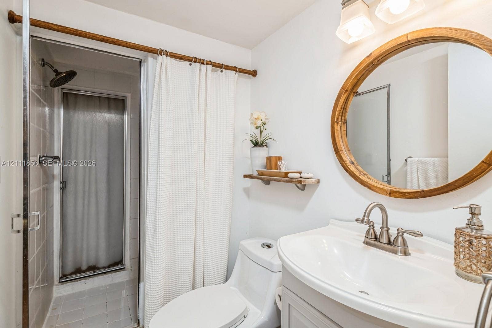 6423 Collins Avenue, #1602, Miami Beach, FL 33141 Bathroom featuring a vanity with an integrated basin, oval wood-frame mirror, wall-mounted floating shelf, and a shower enclosure with tile surround and fixed shower head