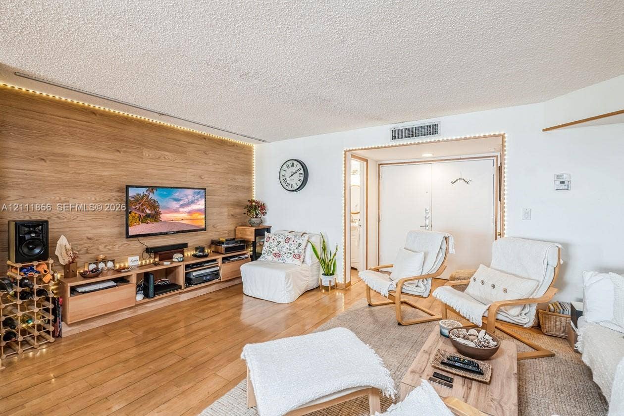 6423 Collins Avenue, #1602, Miami Beach, FL 33141 Living area featuring wood-finish flooring, a wood-paneled accent wall with integrated ambient lighting, and a built-in media console