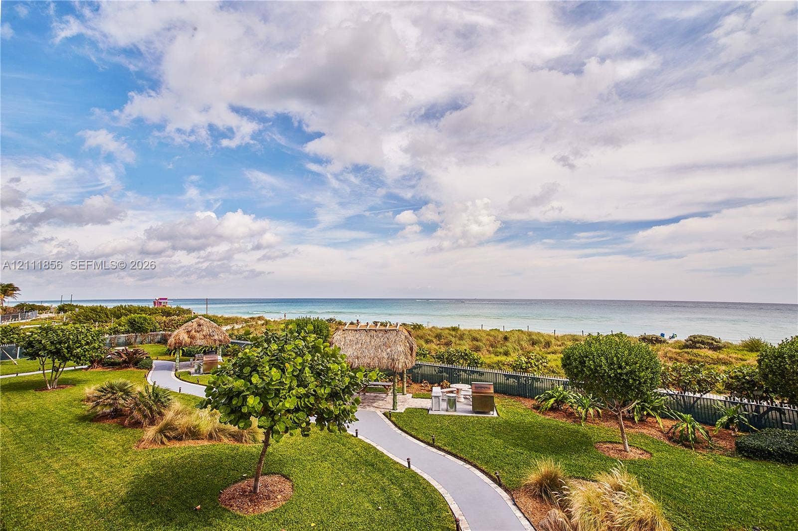 6423 Collins Avenue, #1602, Miami Beach, FL 33141 Coastal grounds featuring manicured lawns, mature landscaping, paved pathways, and multiple thatched-roof structures