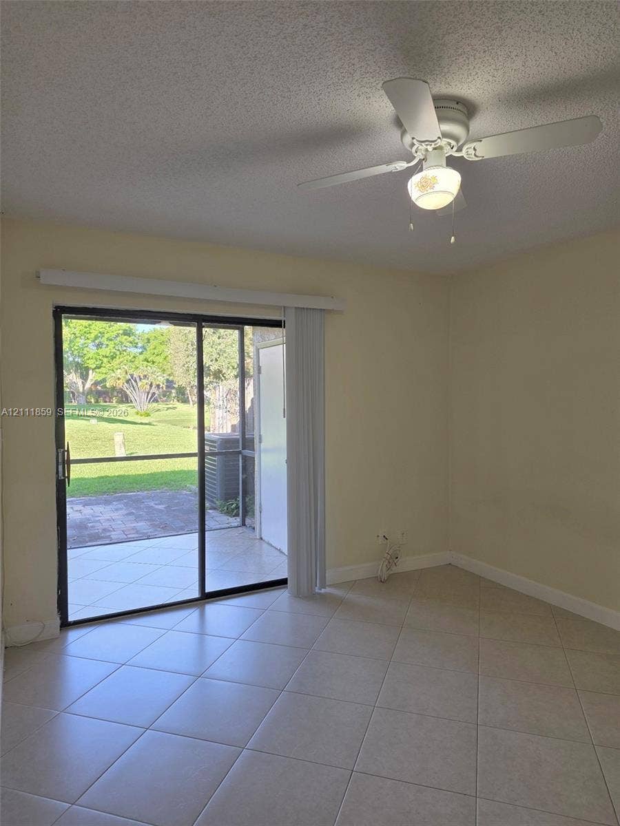 Interior space featuring diagonal ceramic tile flooring, a white ceiling fan with integrated lighting, and a sliding glass door opening to a paved, screened-in patio