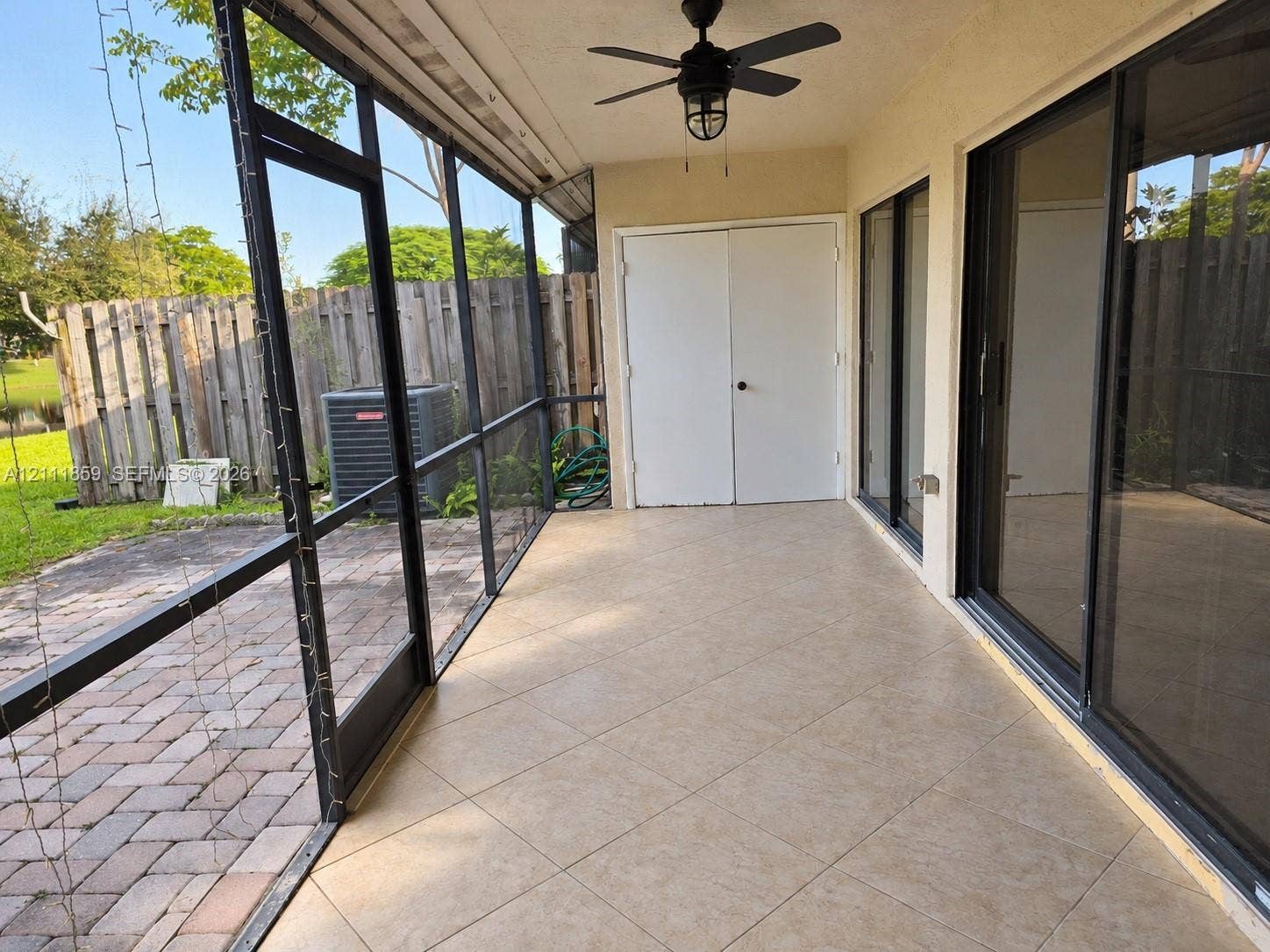 Screened-in patio featuring tile flooring, dual glass sliding doors, a ceiling fan, and double-door storage