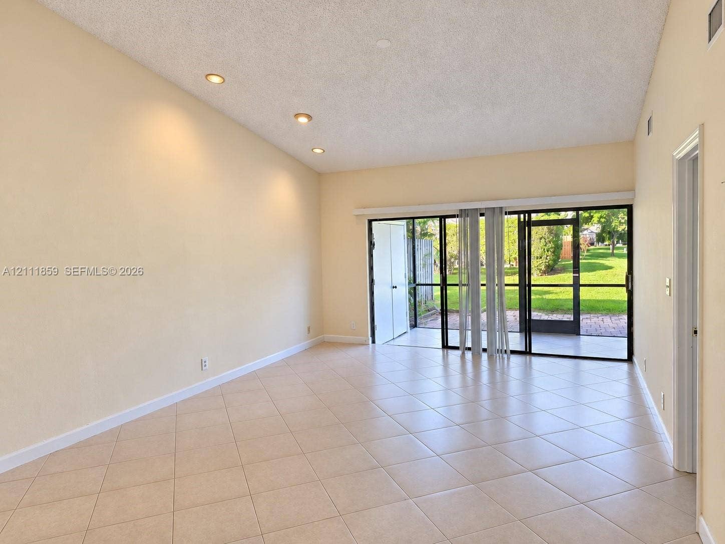 Interior featuring vaulted ceilings, recessed lighting, tile flooring, and large sliding glass doors providing access to a screened-in patio