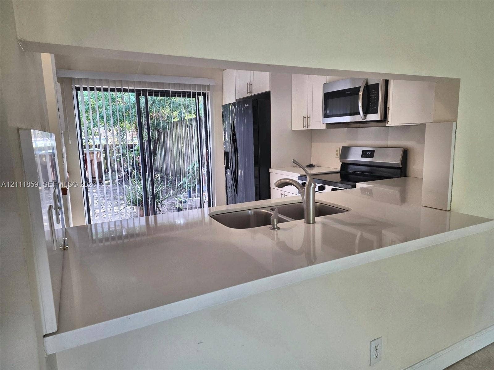 Kitchen featuring white cabinetry, solid-surface countertops, dual-basin stainless steel sink with high-arc faucet, and built-in stainless steel appliances