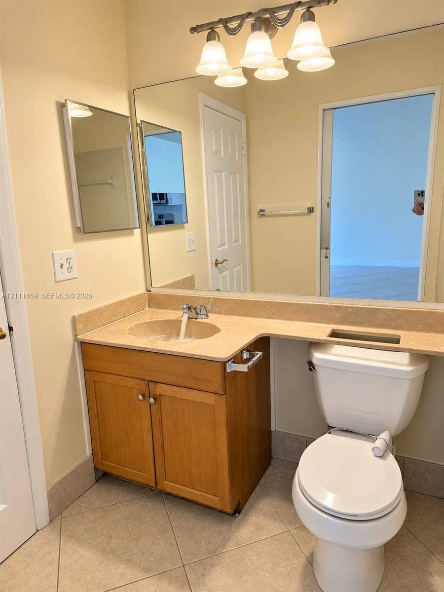 Vanity cabinet with wood-finish cabinetry, stone-surfaced countertop with integrated sink, large wall-mounted mirror, and multi-bulb fixture