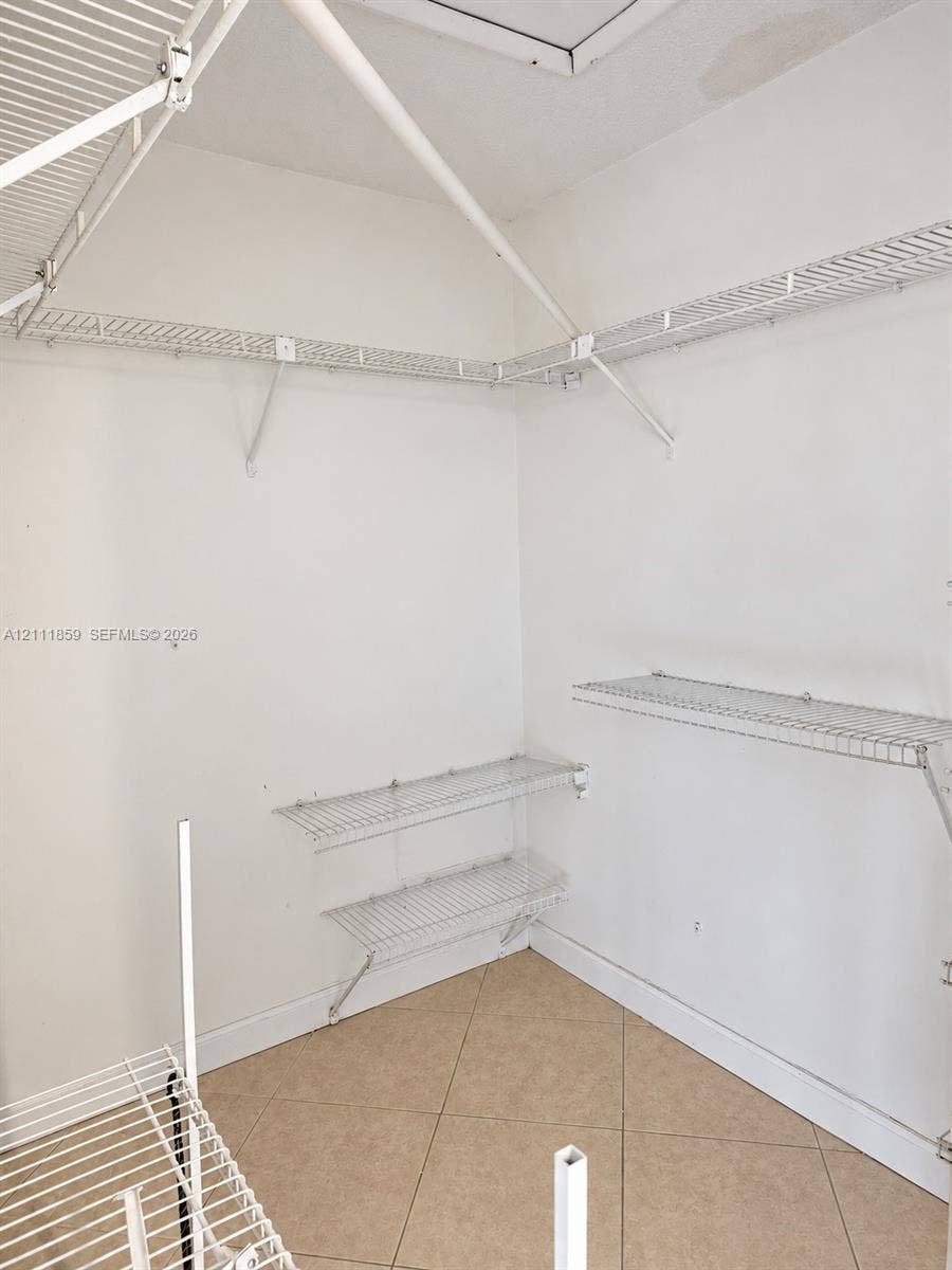 Storage space featuring white wire shelving units and neutral tile flooring