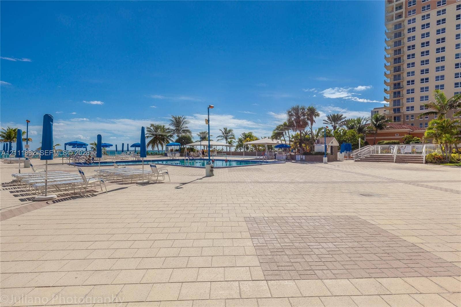 2030 S Ocean Drive, #2004, Hallandale Beach, FL 33009 Outdoor swimming pool surrounded by a paved deck, shaded structures, and lush palm trees