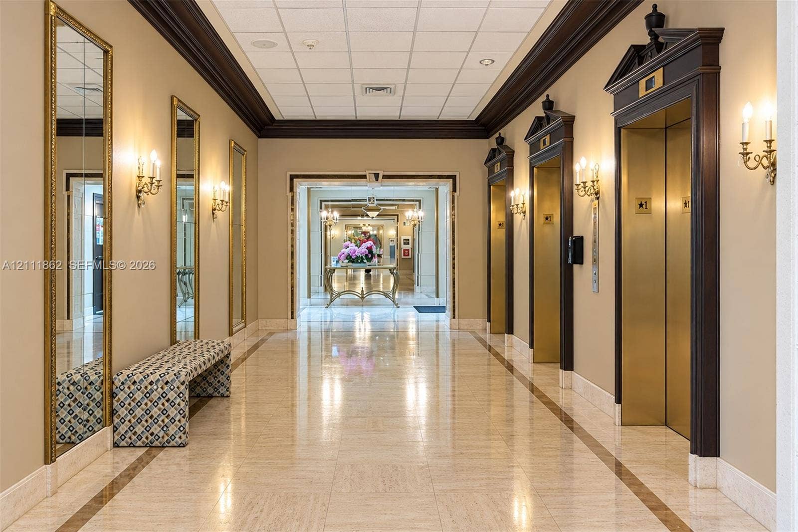 2030 S Ocean Drive, #2004, Hallandale Beach, FL 33009 Formal corridor featuring polished stone flooring, custom dark-wood elevator surrounds with architectural pediments, integrated wall-mounted sconces, and full-length framed mirrors