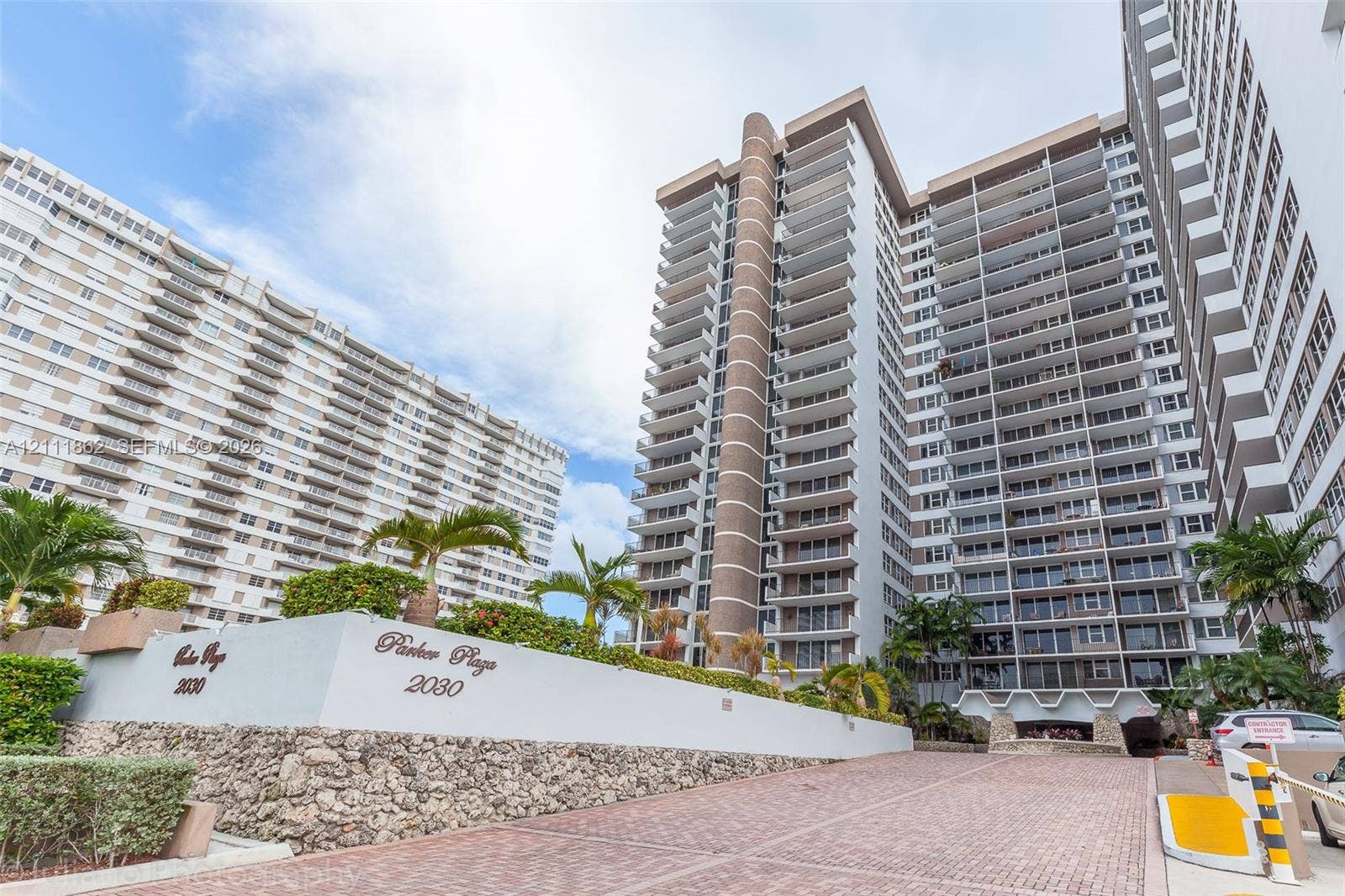 2030 S Ocean Drive, #2004, Hallandale Beach, FL 33009 High-rise exterior featuring multi-level private balconies, masonry facade detailing, natural stone-faced retaining walls, paved motor court, and tropical landscaping