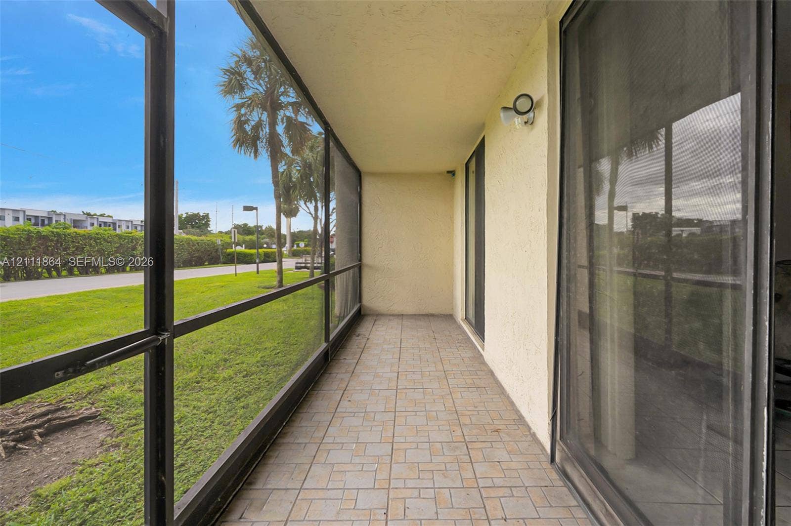 6195 Rock Island Road, #104, Tamarac, FL 33319 Screened-in porch featuring tile flooring, textured wall finishes, and an attached exterior light fixture