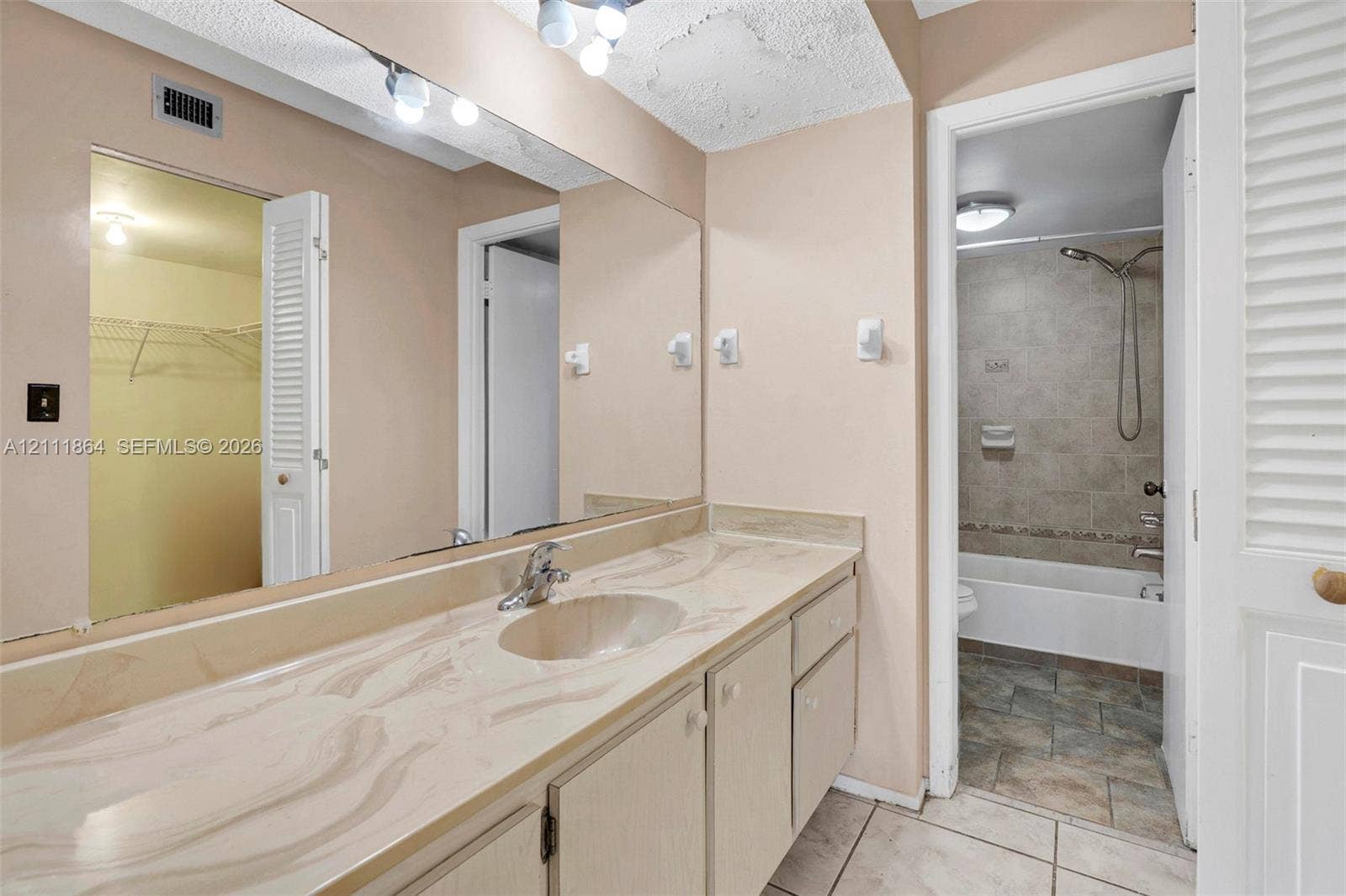 6195 Rock Island Road, #104, Tamarac, FL 33319 Bathroom vanity featuring a solid surface countertop with integrated basin, full-width wall mirror, wood-finish cabinetry, and tiled flooring