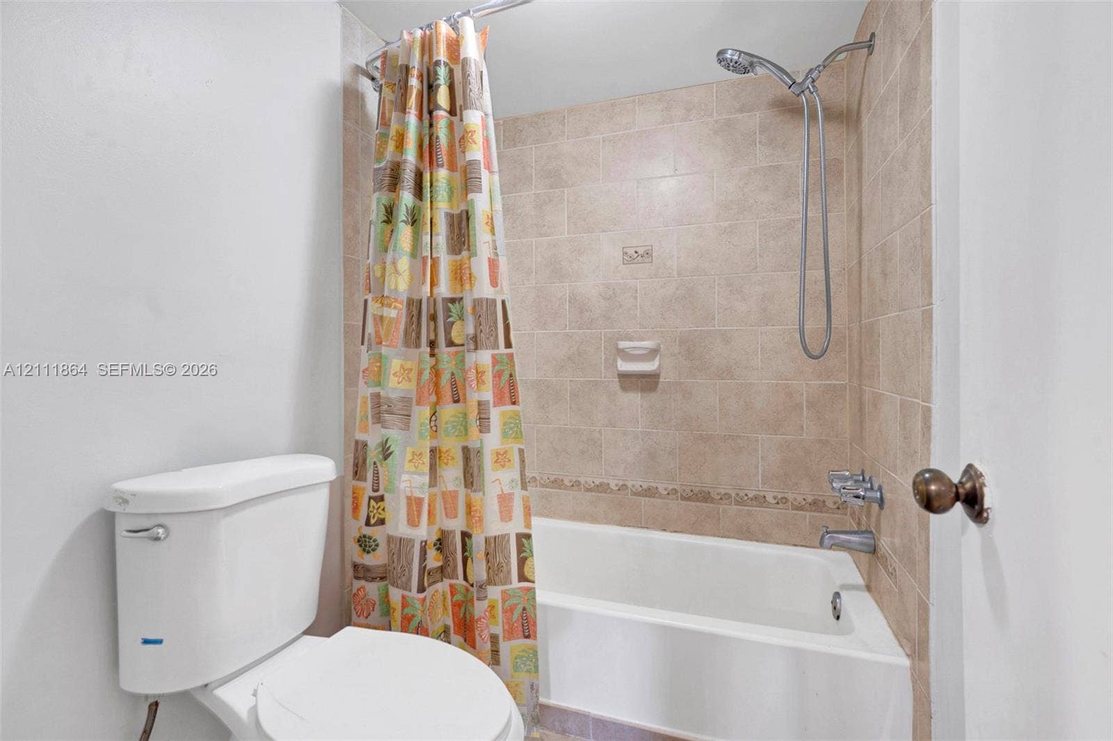 6195 Rock Island Road, #104, Tamarac, FL 33319 Bathroom featuring a porcelain tub, beige tile surround with a decorative inlay, a wall-mounted soap dish, and a chrome hand-held shower fixture