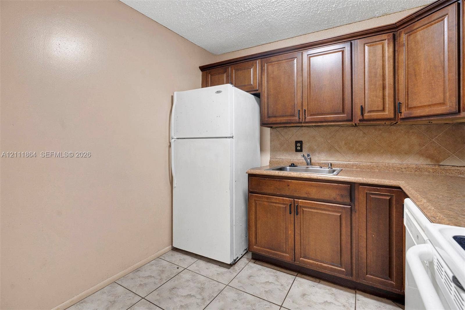 6195 Rock Island Road, #104, Tamarac, FL 33319 Kitchenette featuring wood cabinetry, solid surface countertops, tile backsplash, stainless steel sink, and ceramic tile flooring