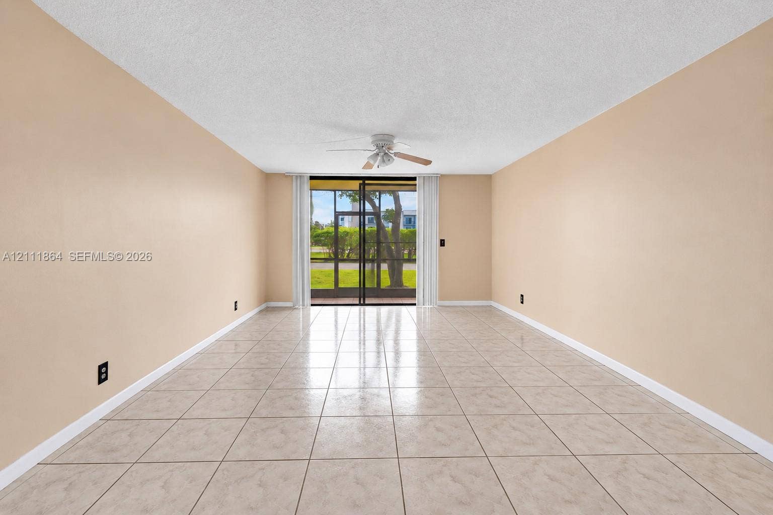 6195 Rock Island Road, #104, Tamarac, FL 33319 Neutral-toned interior featuring ceramic tile flooring, a central ceiling fan, and sliding glass doors